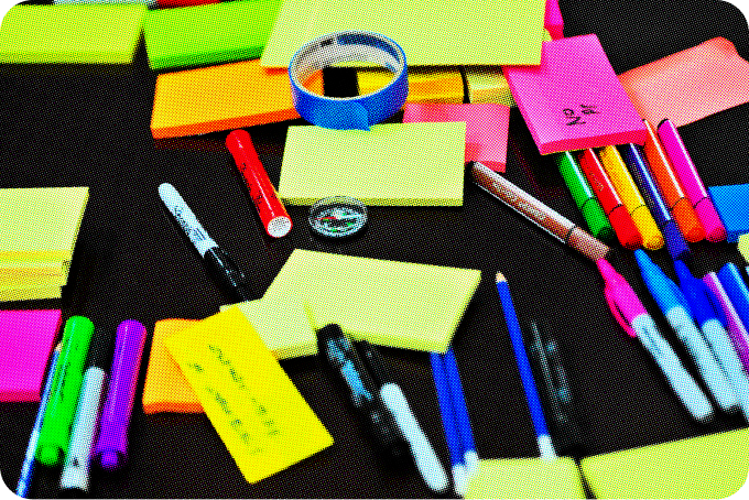 Colorful sticky notes and pens sit on a dark table. 