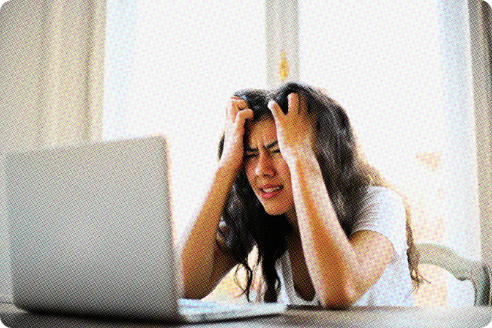 Woman with her hands on her forehead looking frustrated while staring at her computer.