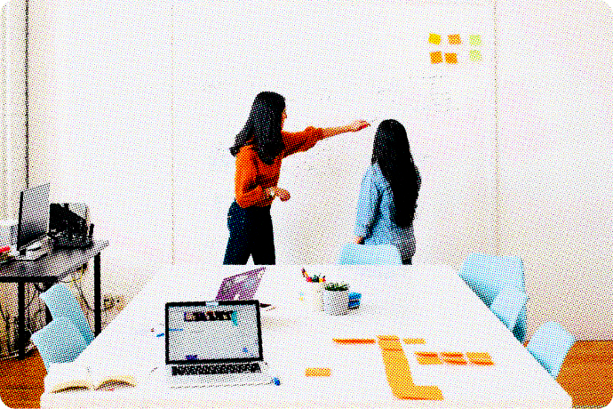 Two women pointing at a white board. 